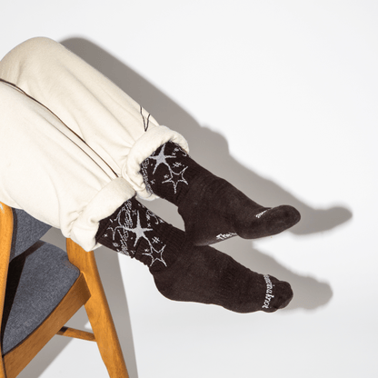 Person wearing black socks with white patterns sitting on a chair against a white background